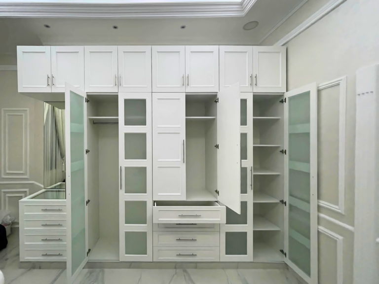 Walk-in wardrobe with glass doors, shelves and central drawer unit by Al Malek Carpentry, Ras Al Khaimah