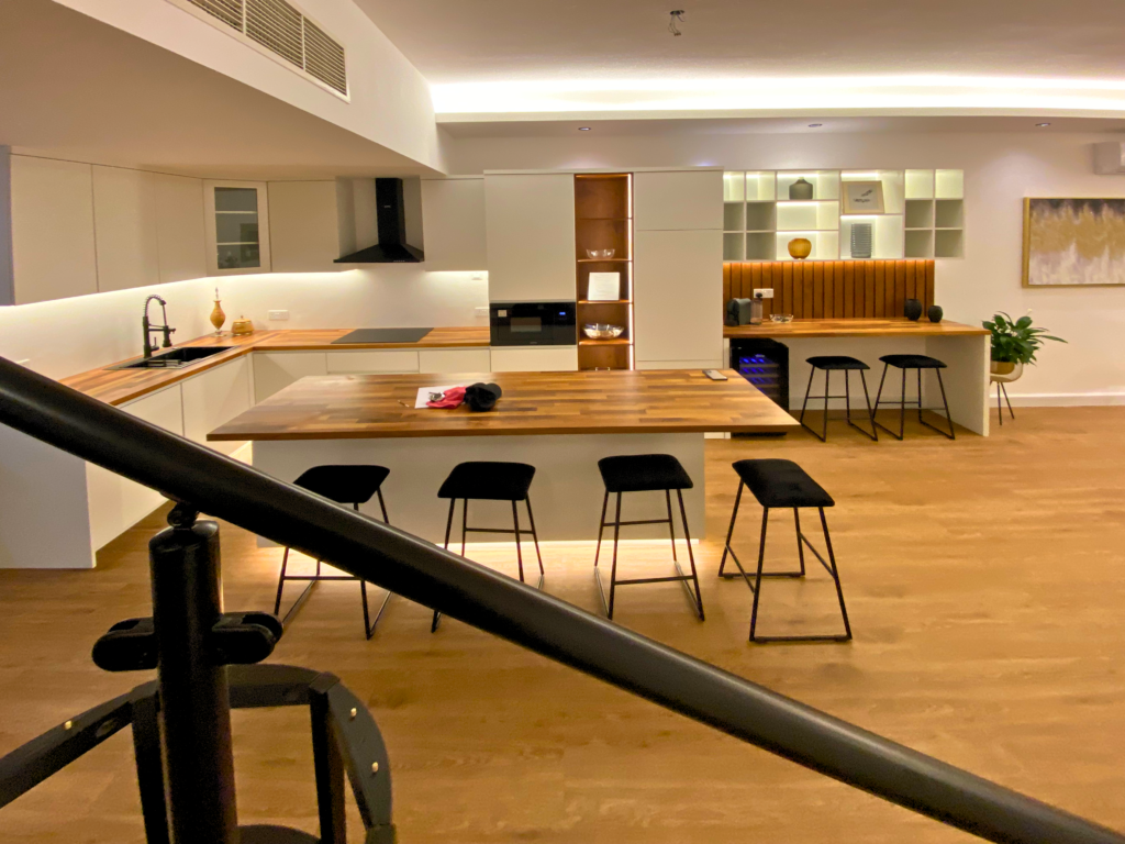 Open-plan kitchen with wooden dining island and bar stools by Al Malek Carpentry, Ras Al Khaimah