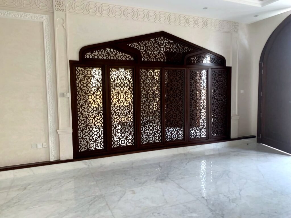 Dark wood CNC mashrabiya wall screen with arched top panels in a villa hall, by Al Malek Carpentry