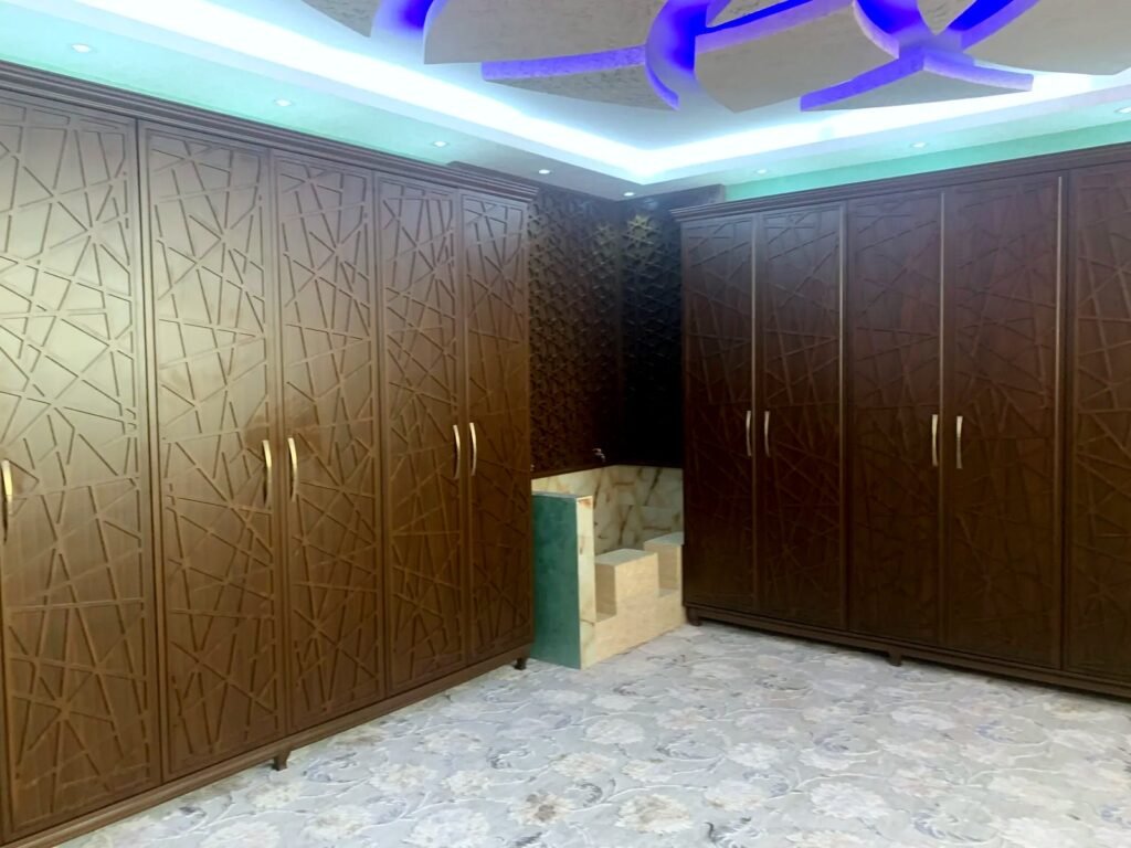Wardrobe wall with CNC-cut geometric pattern doors and a mashrabiya corner panel, made by Al Malek Carpentry