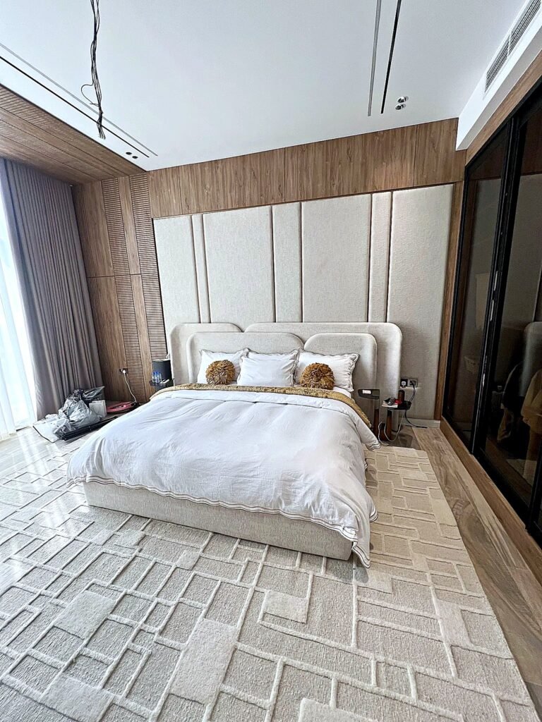 Cream double-layer upholstered king bed with rounded headboard and glass-and-metal side tables in a Ras Al Khaimah villa