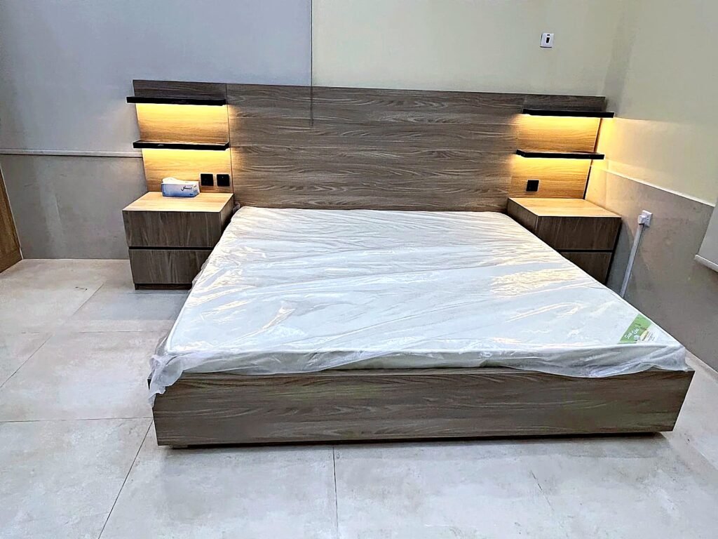 Oak-grain melamine king bed with LED-lit floating shelves and built-in bedside units by Al Malek Carpentry