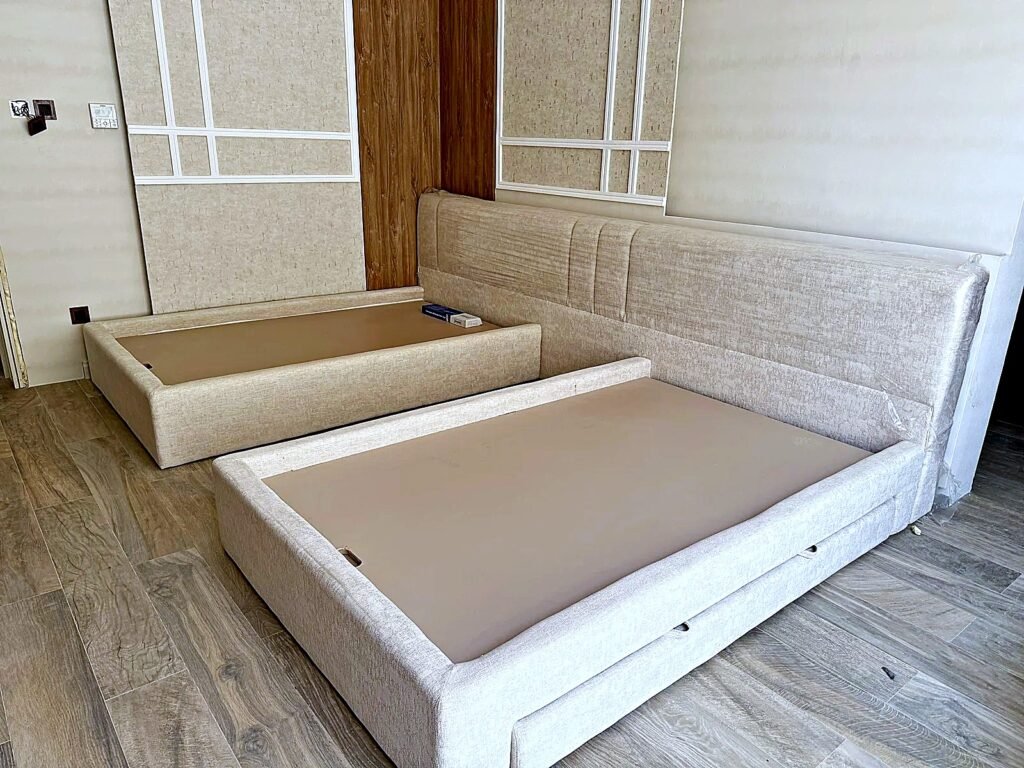 Two 120 x 200 cm upholstered beds with one shared channel-stitched headboard and pull-out storage drawer, before mattresses fitted