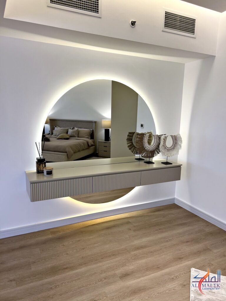Wall-hung dressing table with fluted drawer fronts and a large backlit round mirror in a Bab Al Bahar penthouse by Al Malek Carpentry