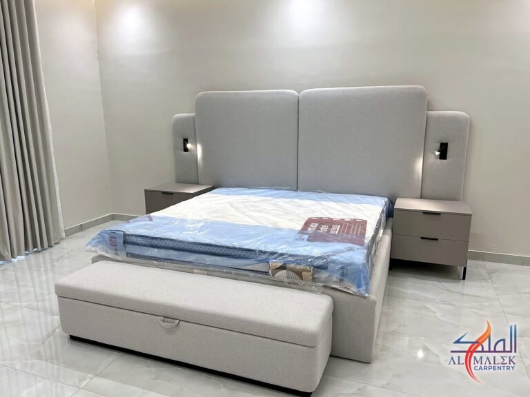 Grey upholstered king bed with double-layer headboard, built-in reading lights and storage ottoman bench by Al Malek Carpentry, Ras Al Khaimah