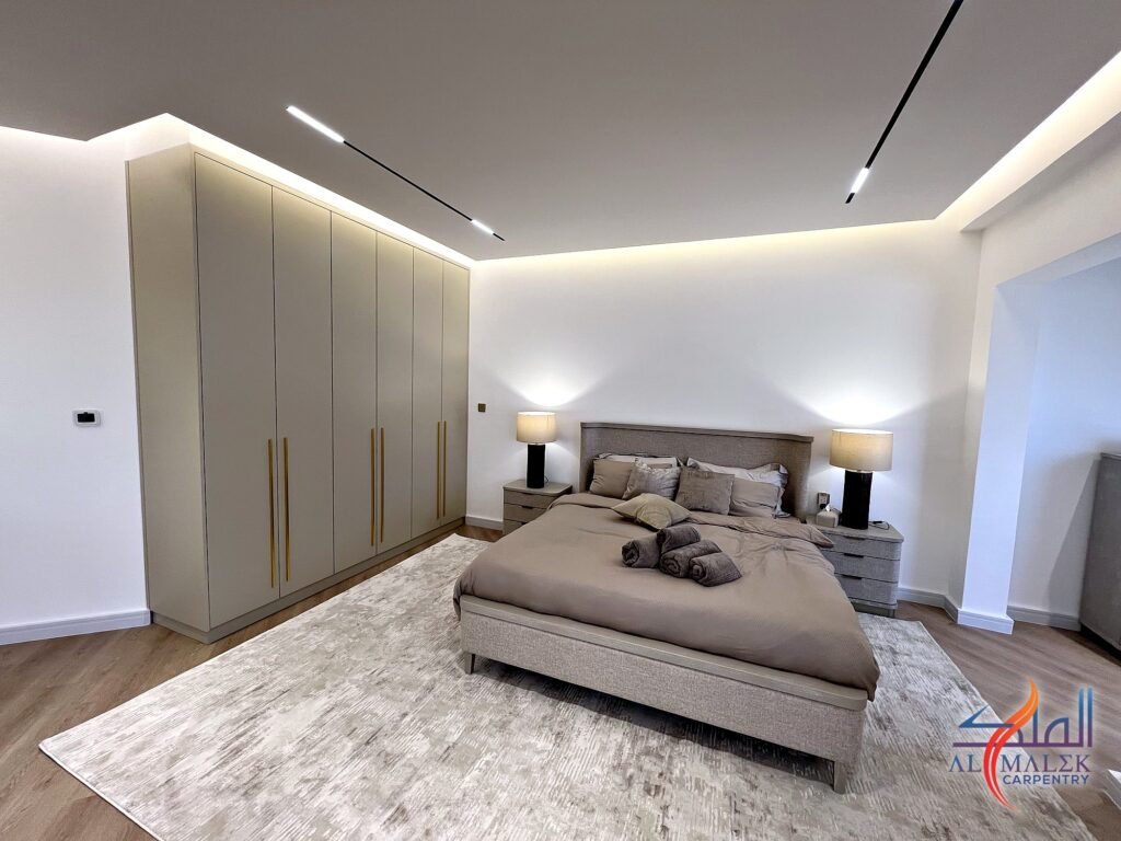 Built-in wardrobe with long gold handles beside an upholstered king bed in a Bab Al Bahar penthouse by Al Malek Carpentry